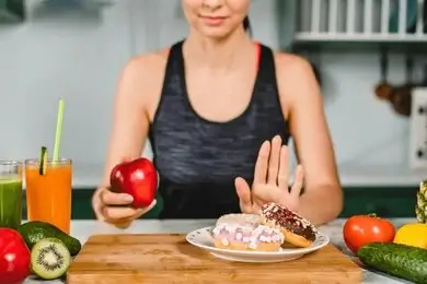 Woman smiling surrounded by fresh fruits and vegetables with sugar sweets in the background symbolizing hormonal balance and sugar impact