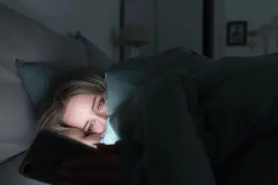 Woman browsing her smartphone at night, exposed to blue light from the screen.