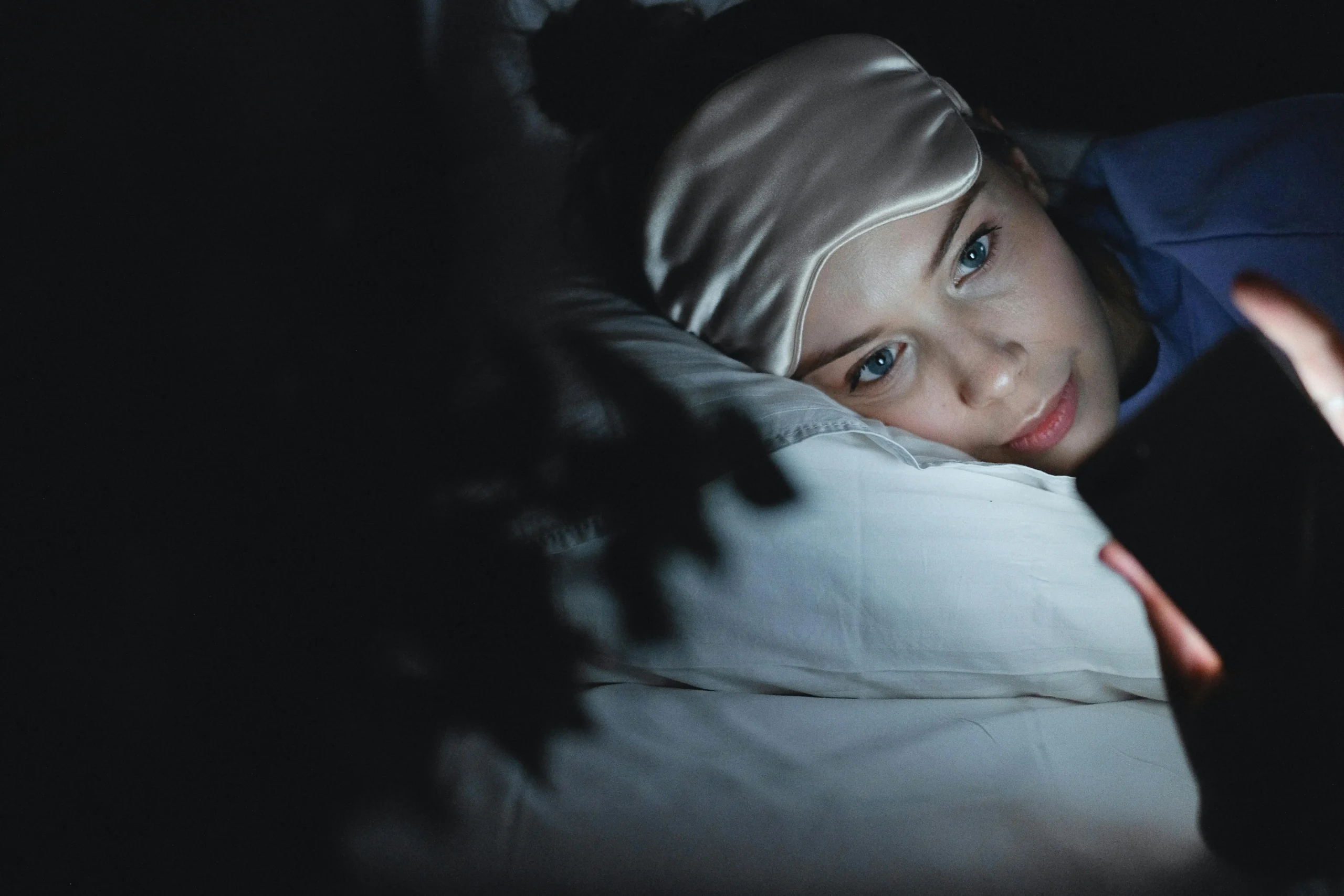 Woman browsing her phone in bed at night with blue light on her face